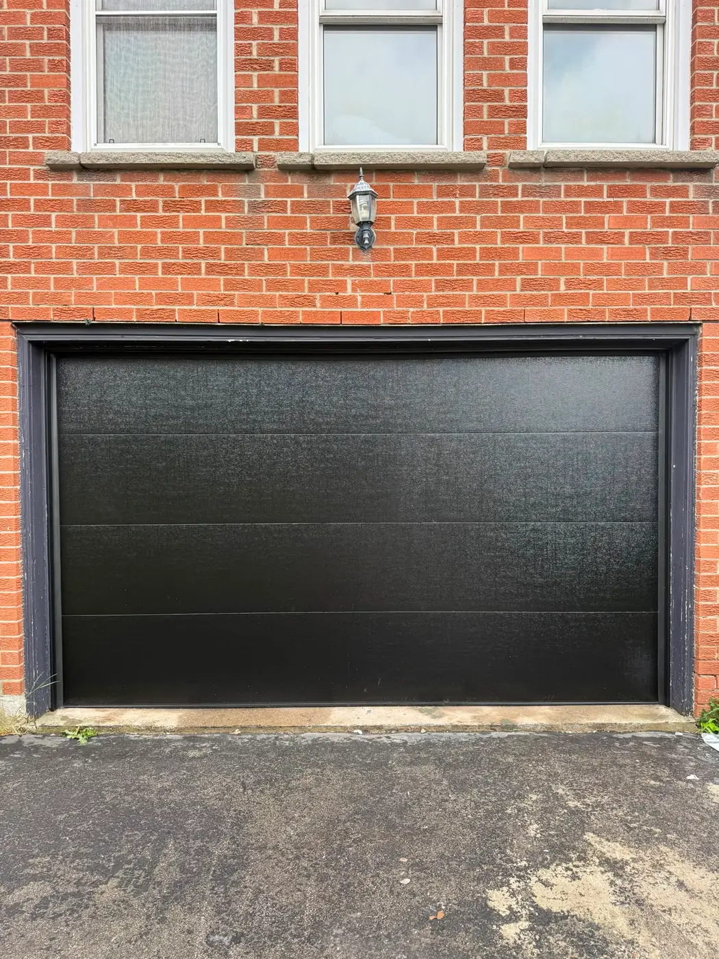 Black flush-panel double garage door on a red brick home