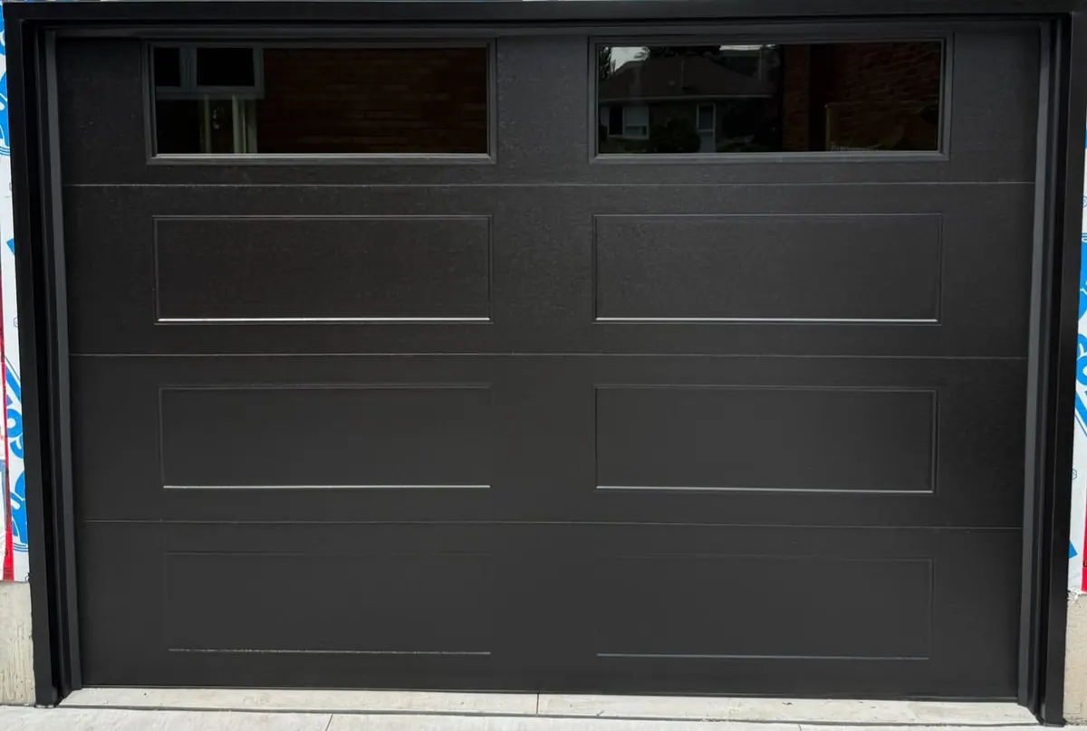 Black long-panel double garage door with top windows on a new build
