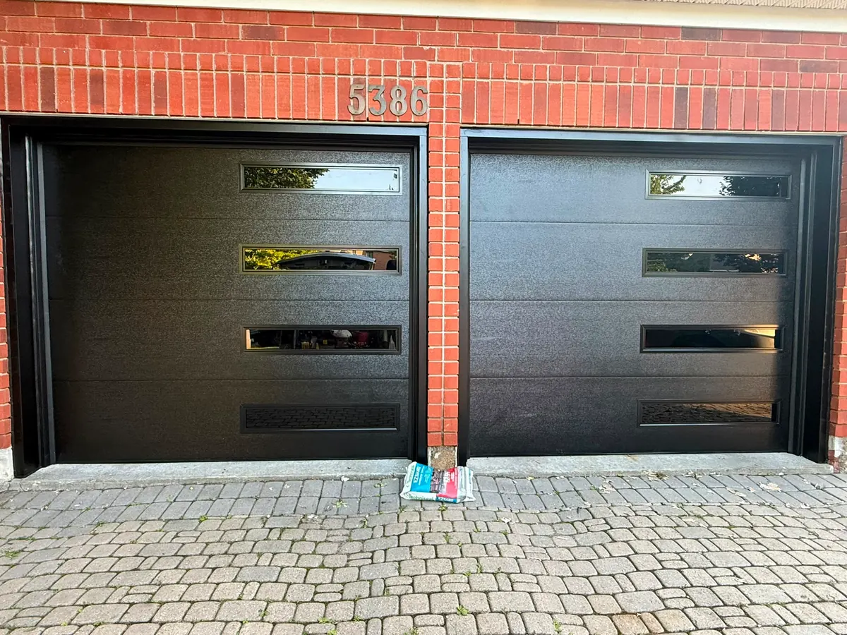 Pair of black modern flush-panel single garage doors on a red brick home