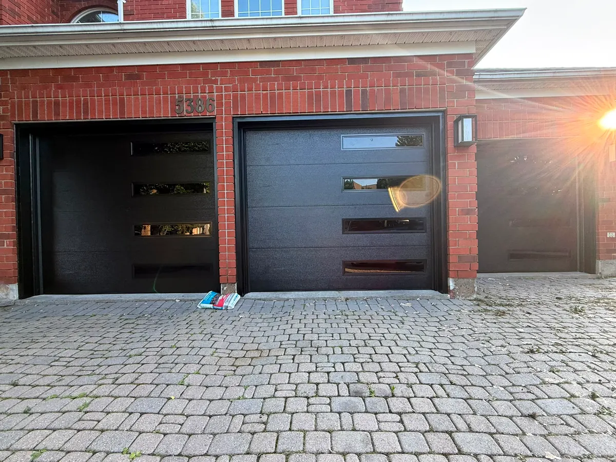 Two black modern flush-panel single garage doors on a brick home