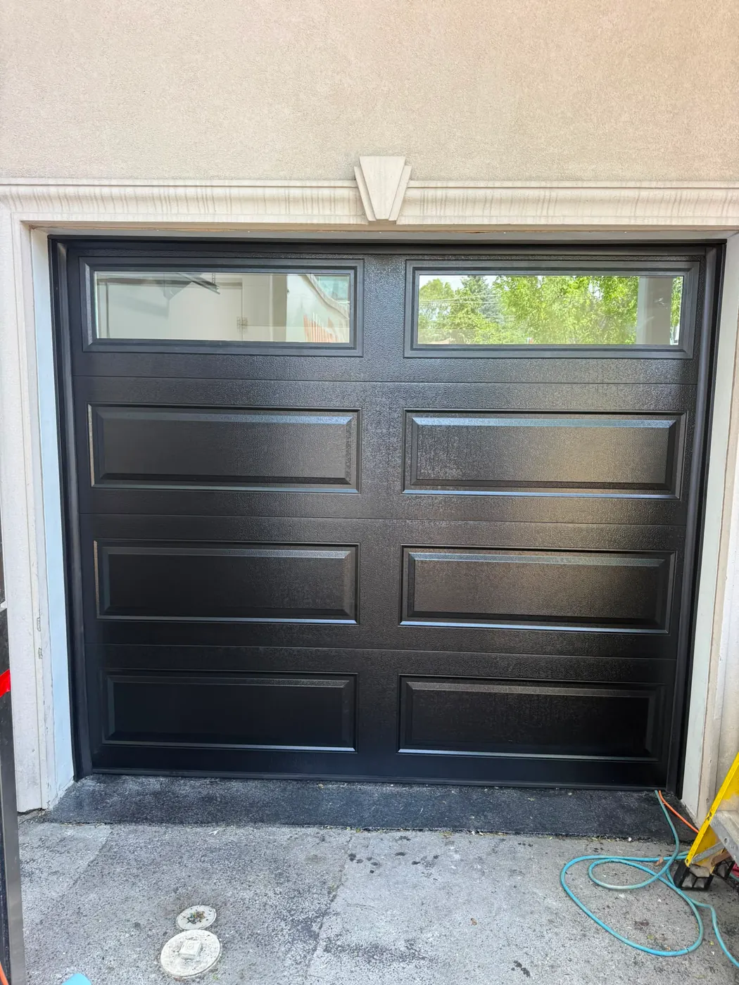 Black raised-panel single garage door with top windows on a stucco home