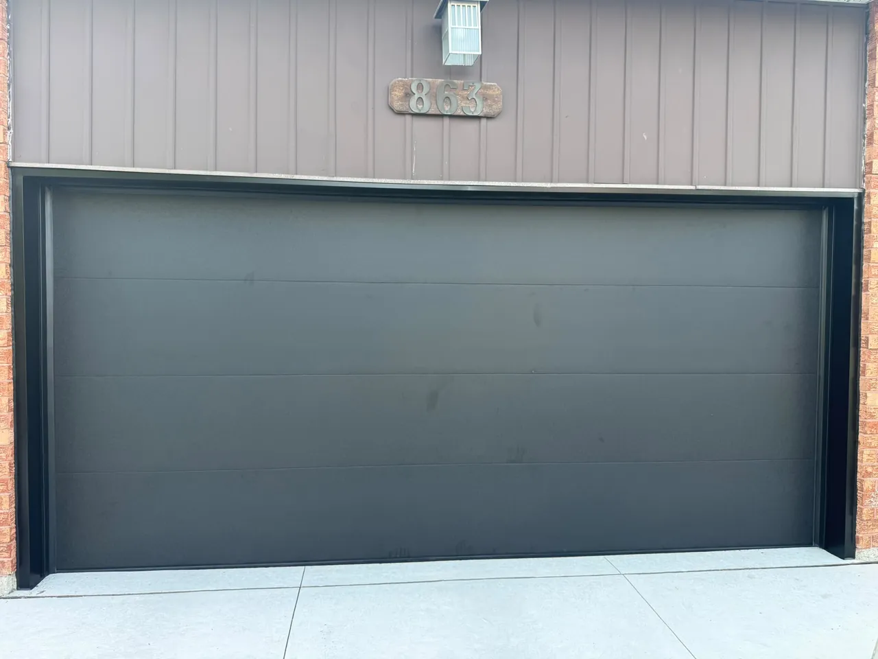 Dark charcoal modern flush-panel garage door on a home with brown siding