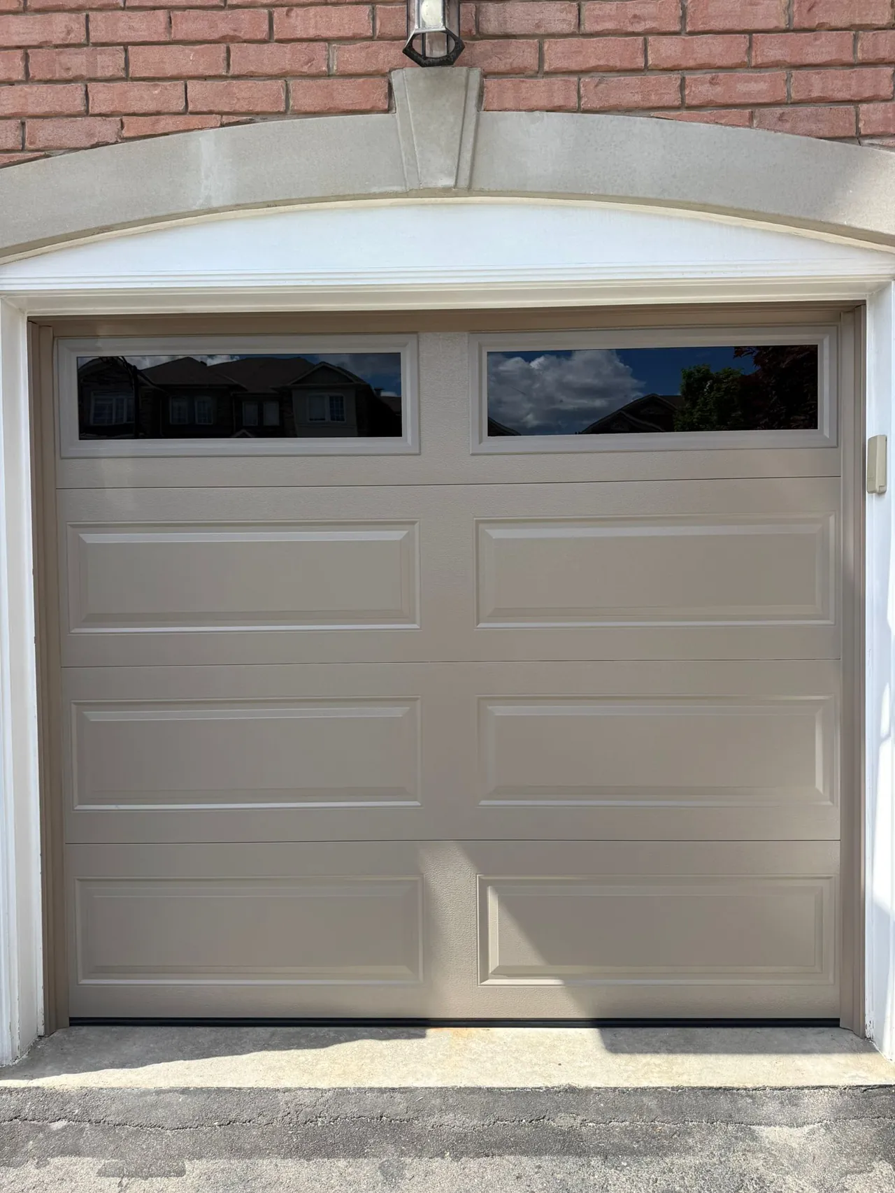 Tan raised-panel garage door with an arched brick surround